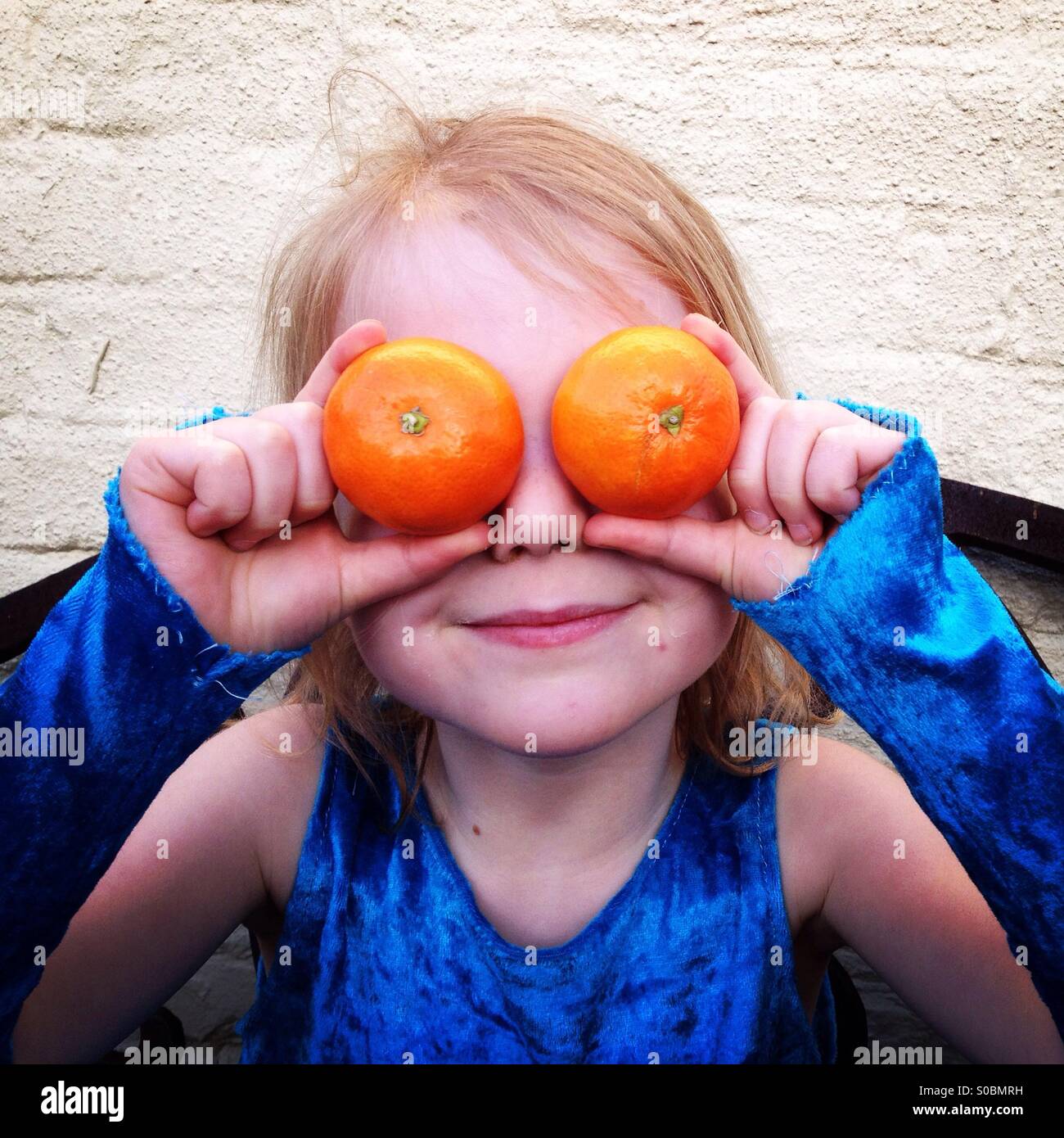 Happy child with oranges as eyes. Girl holding too soft oranges over her eyes. Stock Photo