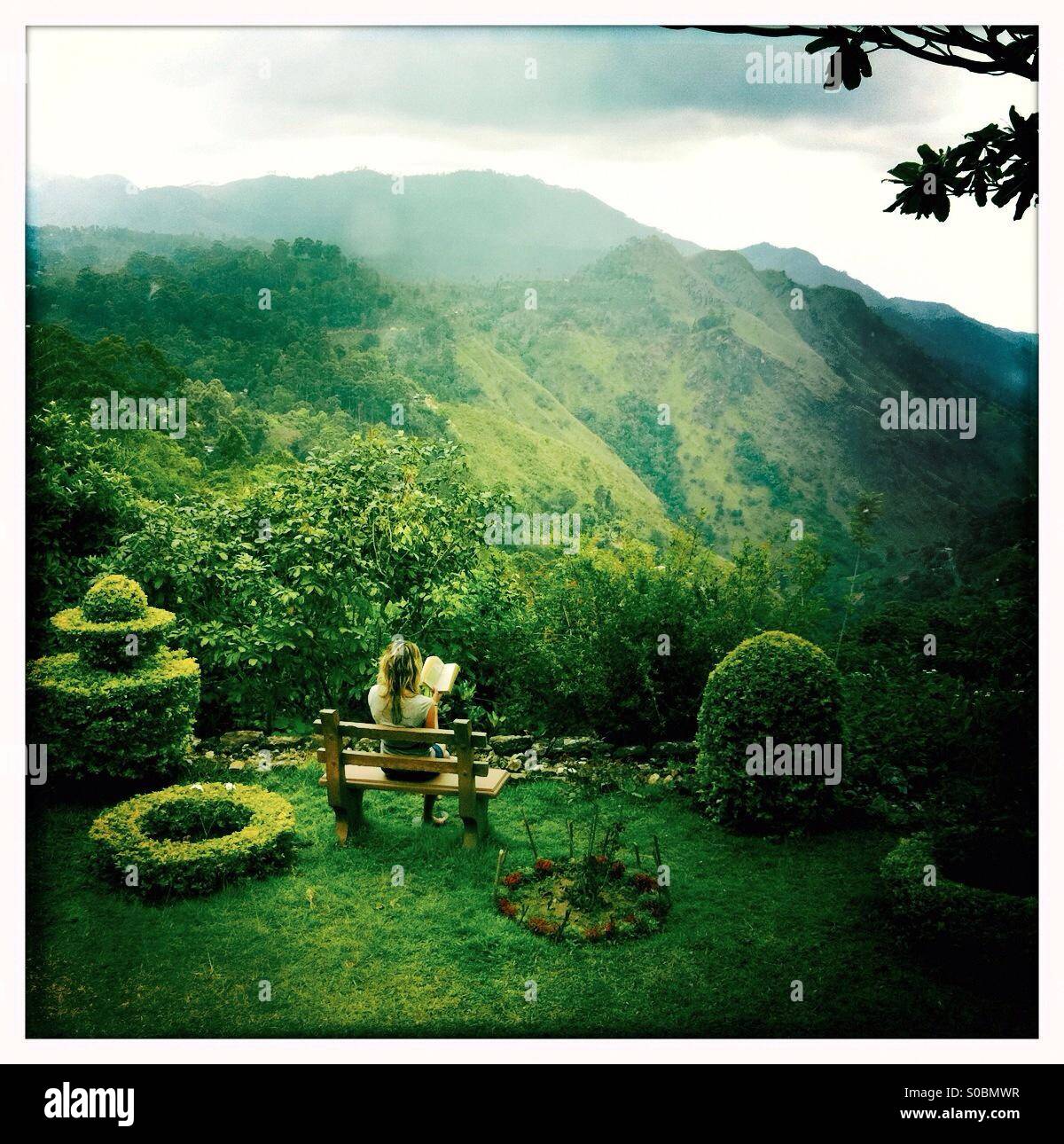 Woman reading a book in a garden with topiary in Ella in Sri Lanka - Smartphone Captured Stock Image