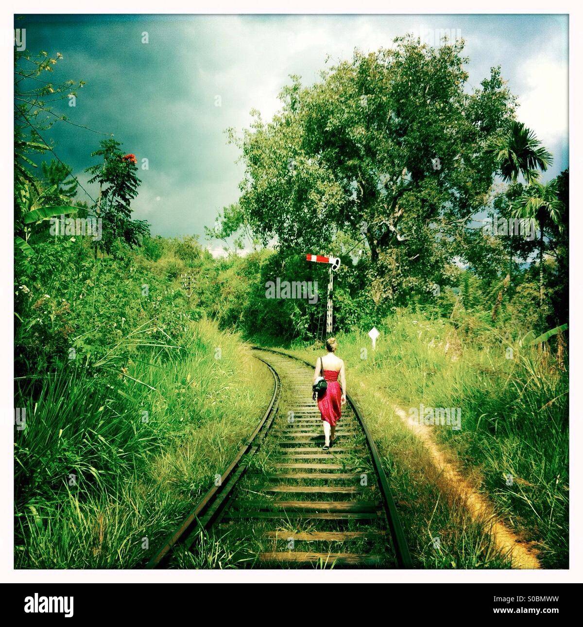 Woman in a red dress walks along a railway line with a signal post in Sri Lanka - Smartphone Captured Stock Image