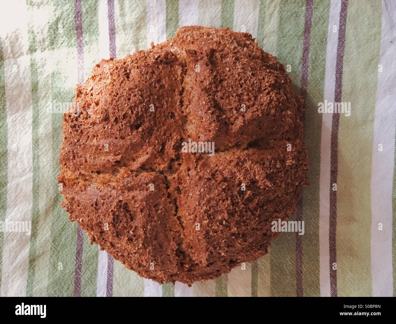 Freshly home made loaf of soda bread cooling on a green and brown striped tea towel. - Smartphone Captured Stock Image