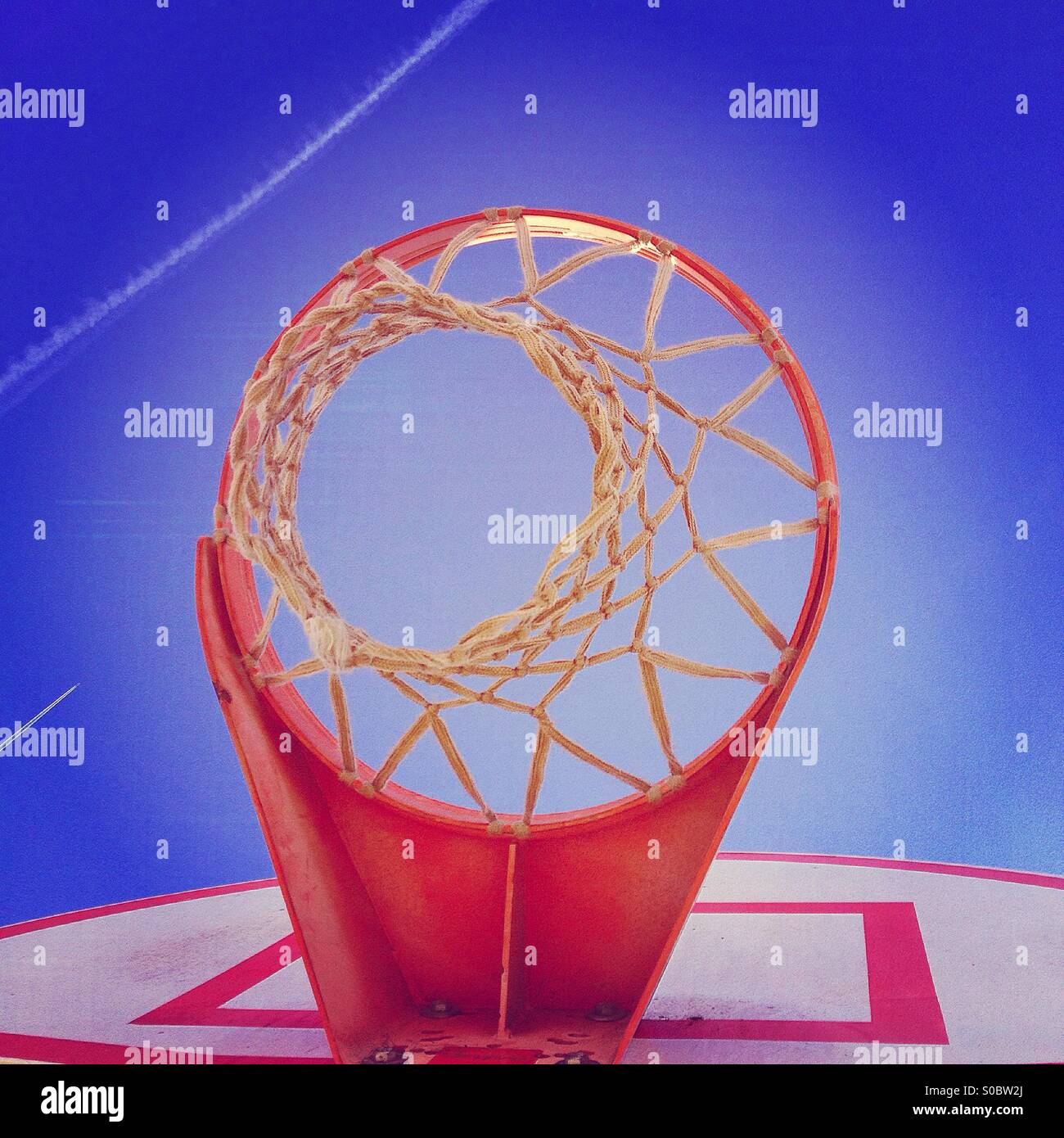 Red basketball hoop and white net against blue sky with plane contrails