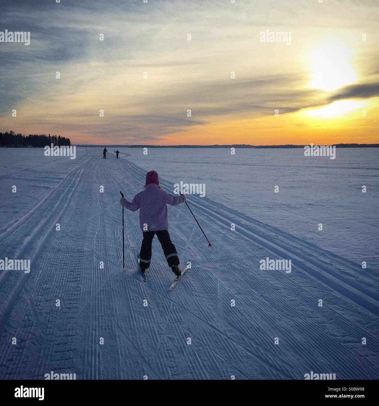 A family skiing on tracks on a frozen lake during a Nordic Scandinavian holiday in Arctic Finland at sunset Stock Photo