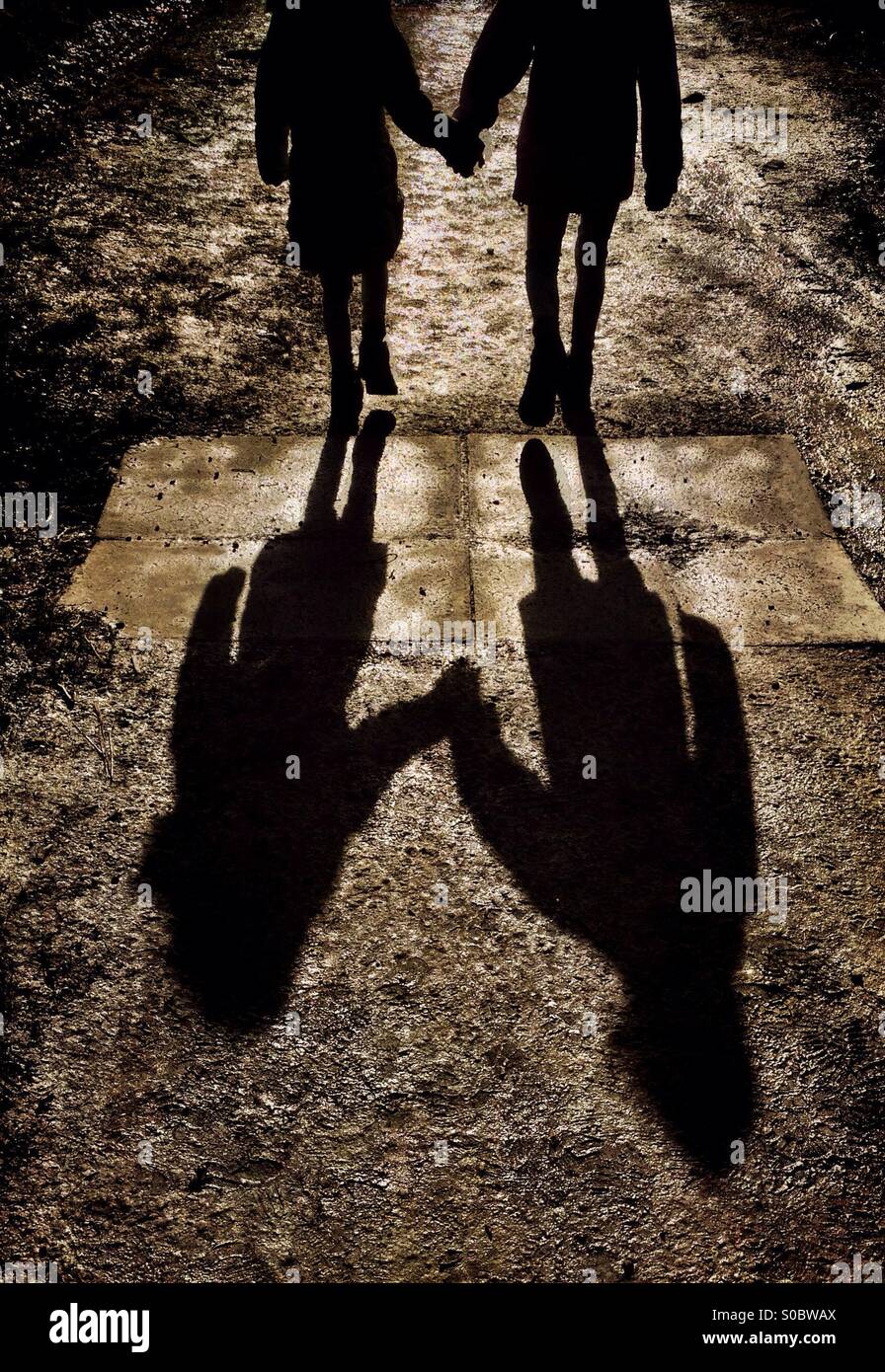 Two young girls walking hand in hand and casting long shadows Stock Photo -  Alamy
