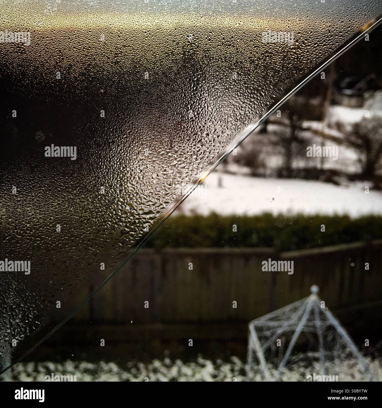A window cracked diagonally from corner to corner in winter with one triangle clear and the other covered in condensation - Smartphone Captured Stock Image