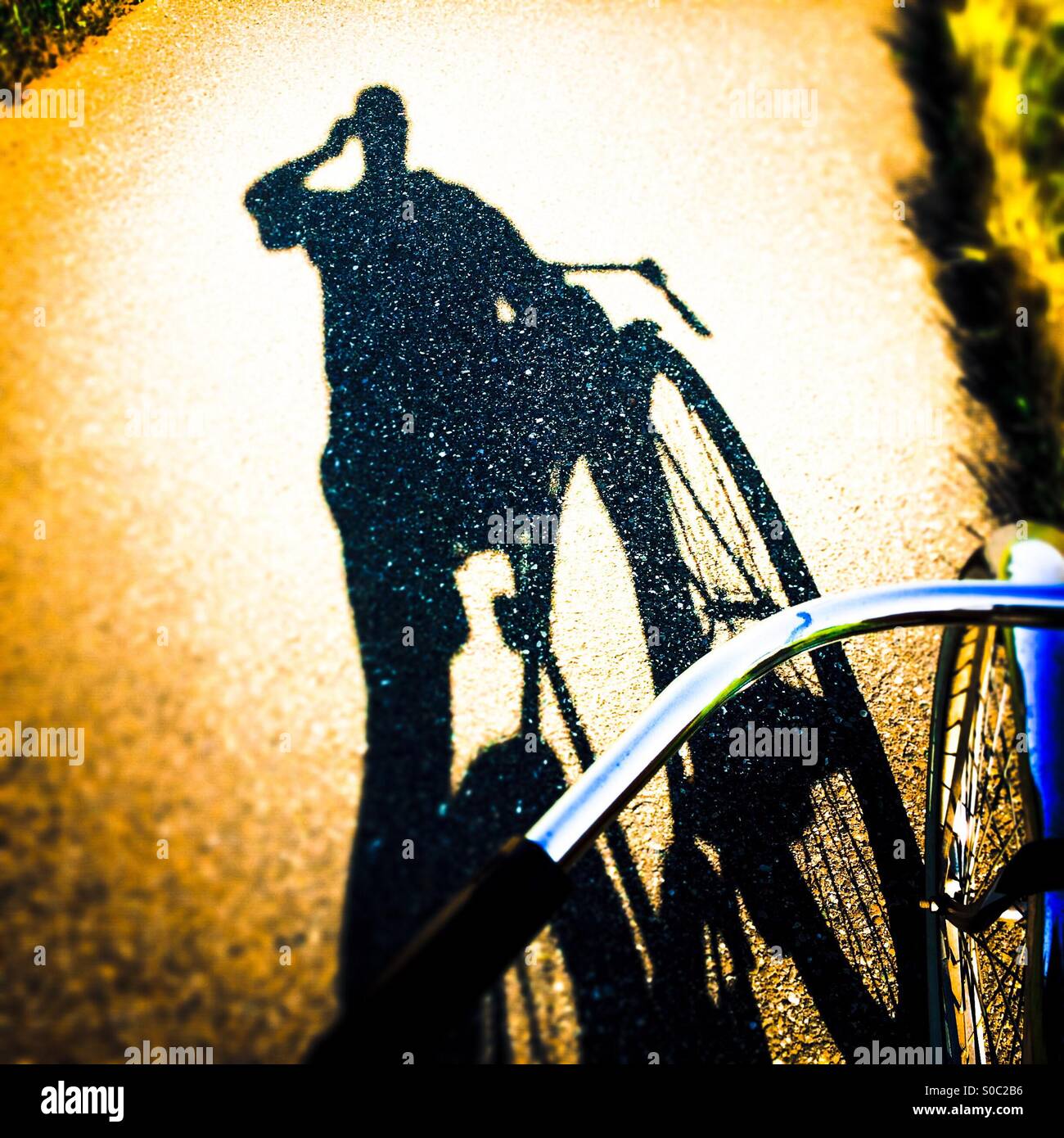 A shadow of a bike rider talking on a cell phone on a bike path. - Smartphone Captured Stock Image