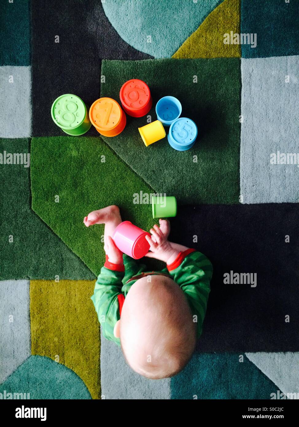 Baby boy plays with stacking cups on a geometric patterned rug Stock Photo