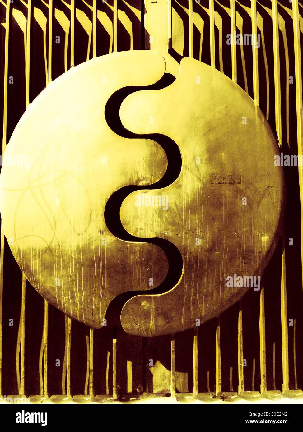 Golden gate. A metal structure with a zig-zag break in a circle as a latch. Glowing in the afternoon sun. Geometry of vertical lines, a circular shape, and a fluid, undulating curve. - Smartphone Captured Stock Image