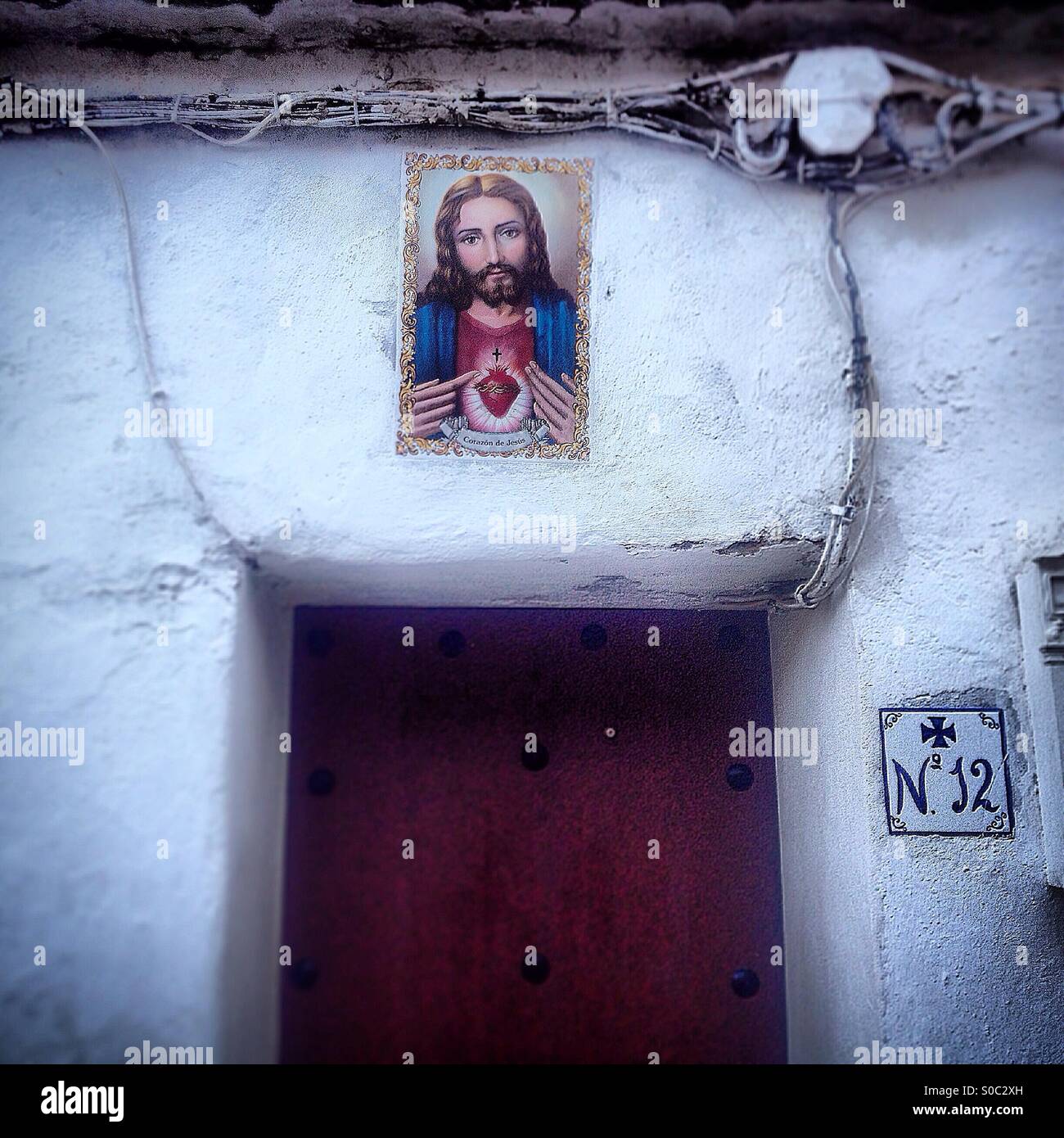A ceramic tile of the Sacred Heart of Jesus decortes a white house in Arcos de la Frontera, Sierra de Cadiz, Andalusia, Spain - Smartphone Captured Stock Image