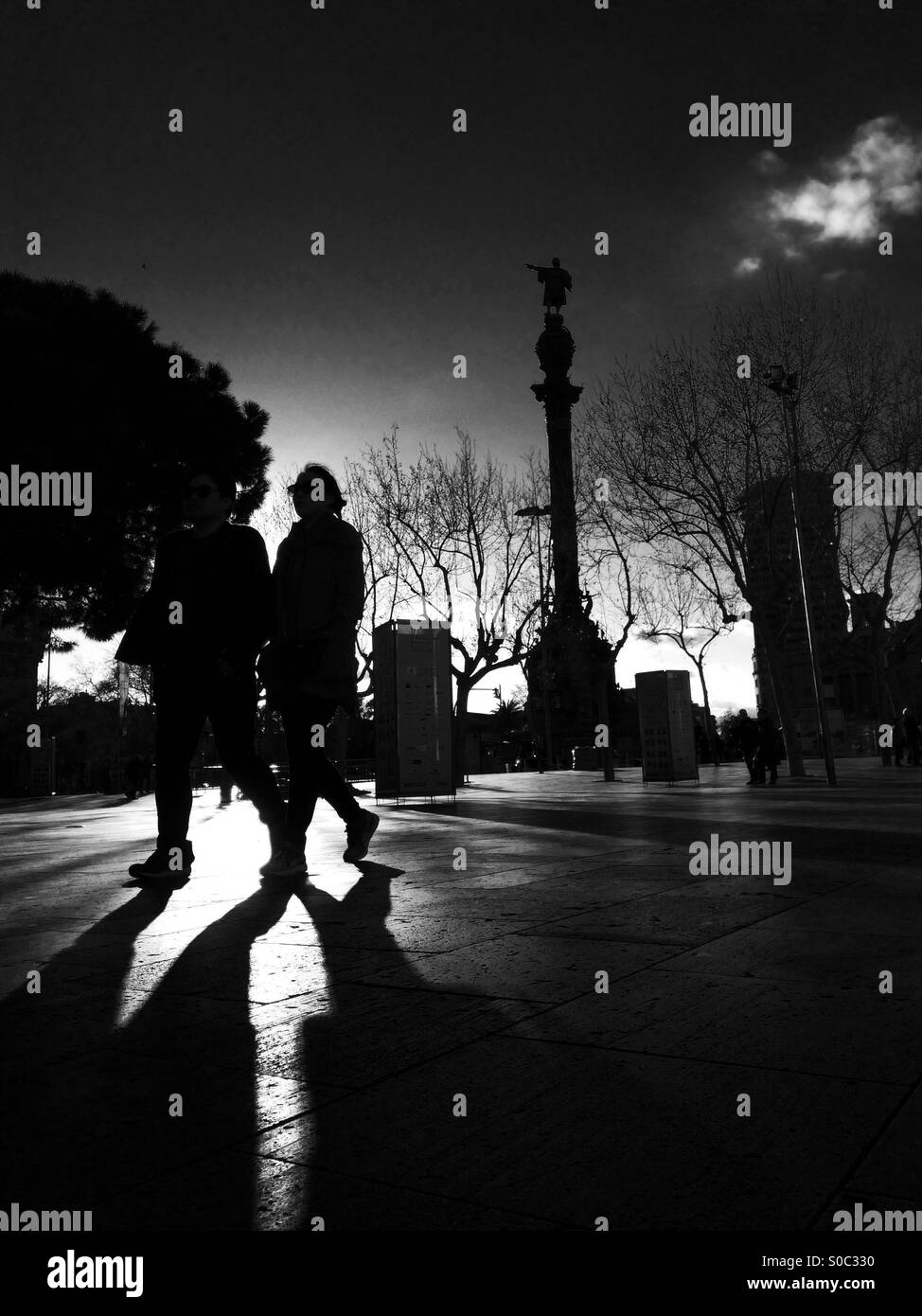 A couple walking by the Mirador de Colom Columbus Monument Barcelona in the late evening sun Stock Photo