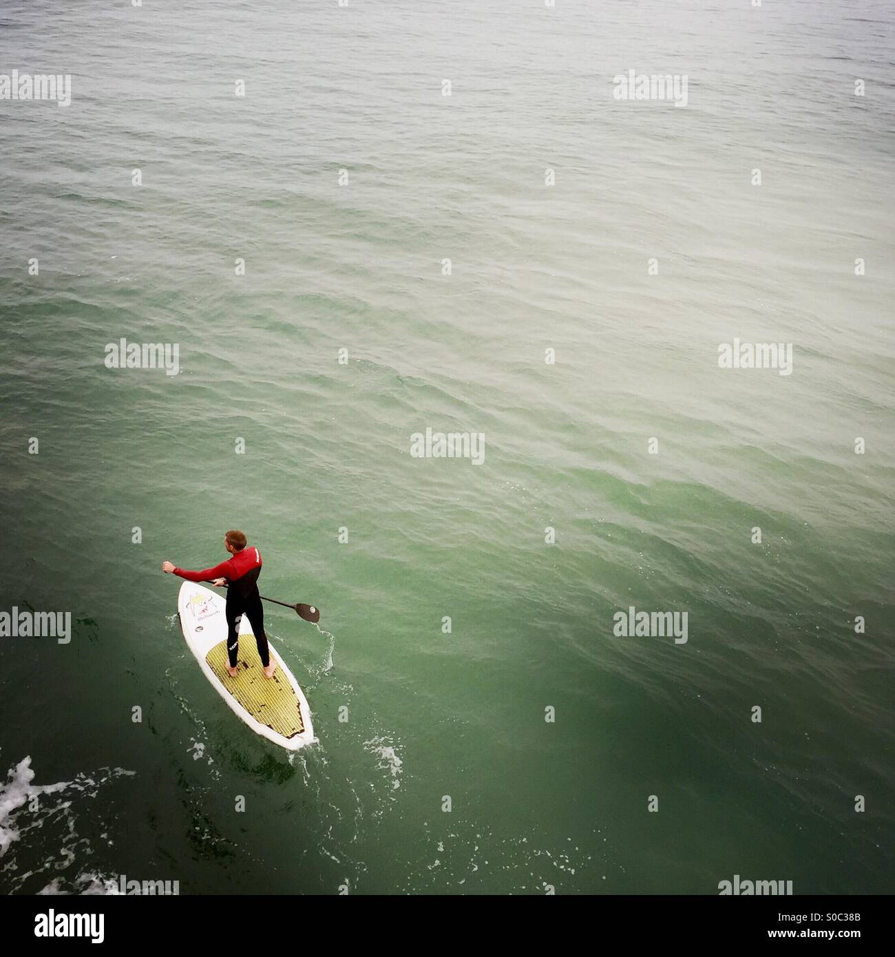 A standup surfer paddles out to the surf. Manhattan beach, California USA. - Smartphone Captured Stock Image
