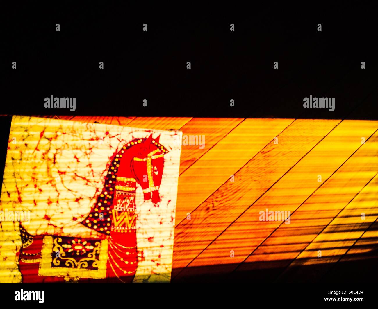 Horse. A batik frame of a decorative, bridled horse glows in golden light. Artisanal, hand made. Cedar panel. - Smartphone Captured Stock Image