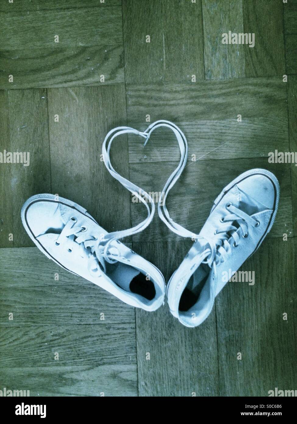 Heart shape in laces with white trainers on a wooden floor. Stock Photo