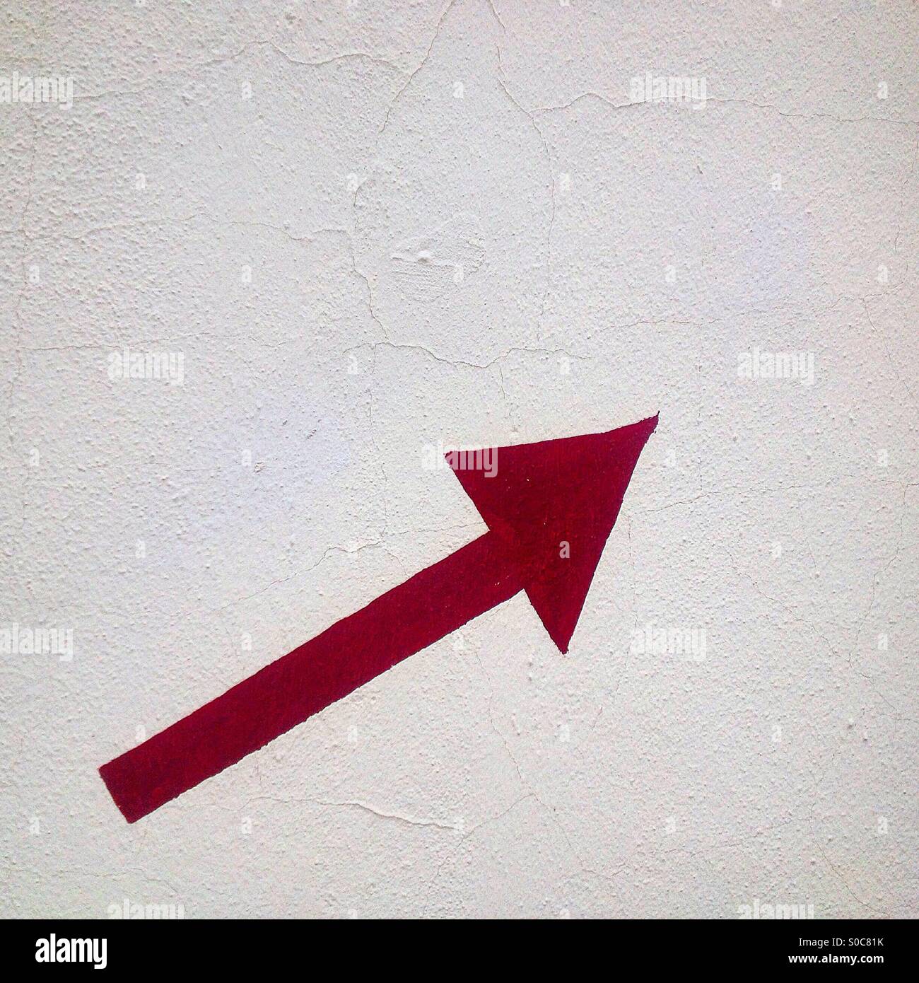A painted red arrow pointing up right decorates a white wall in Medina Sidonia, Cadiz, Andalusia,Spain Stock Photo