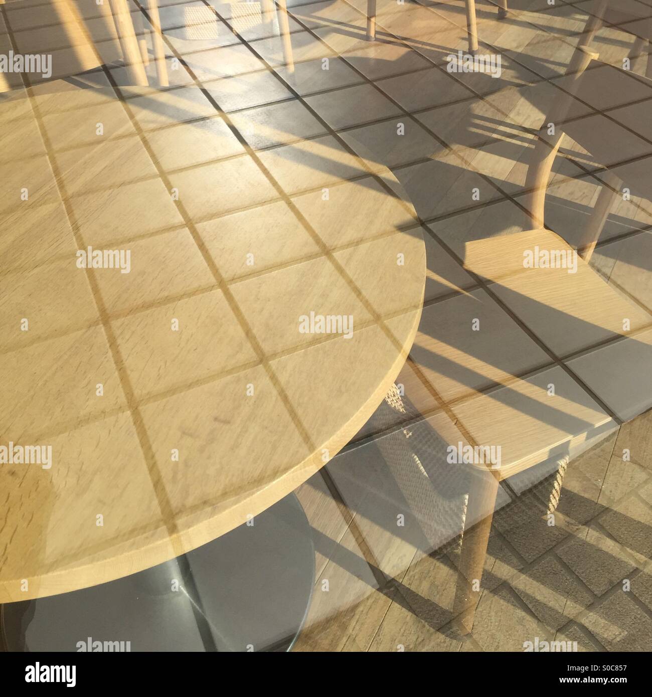 Wooden table and chair seen through glass wall reflecting outdoor tile floor. Stock Photo