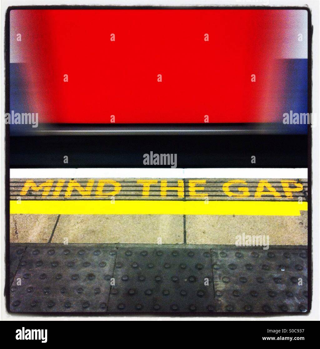 'Mind the gap' warning text in yellow on a London Underground platform, with a moving tube behind. - Smartphone Captured Stock Image