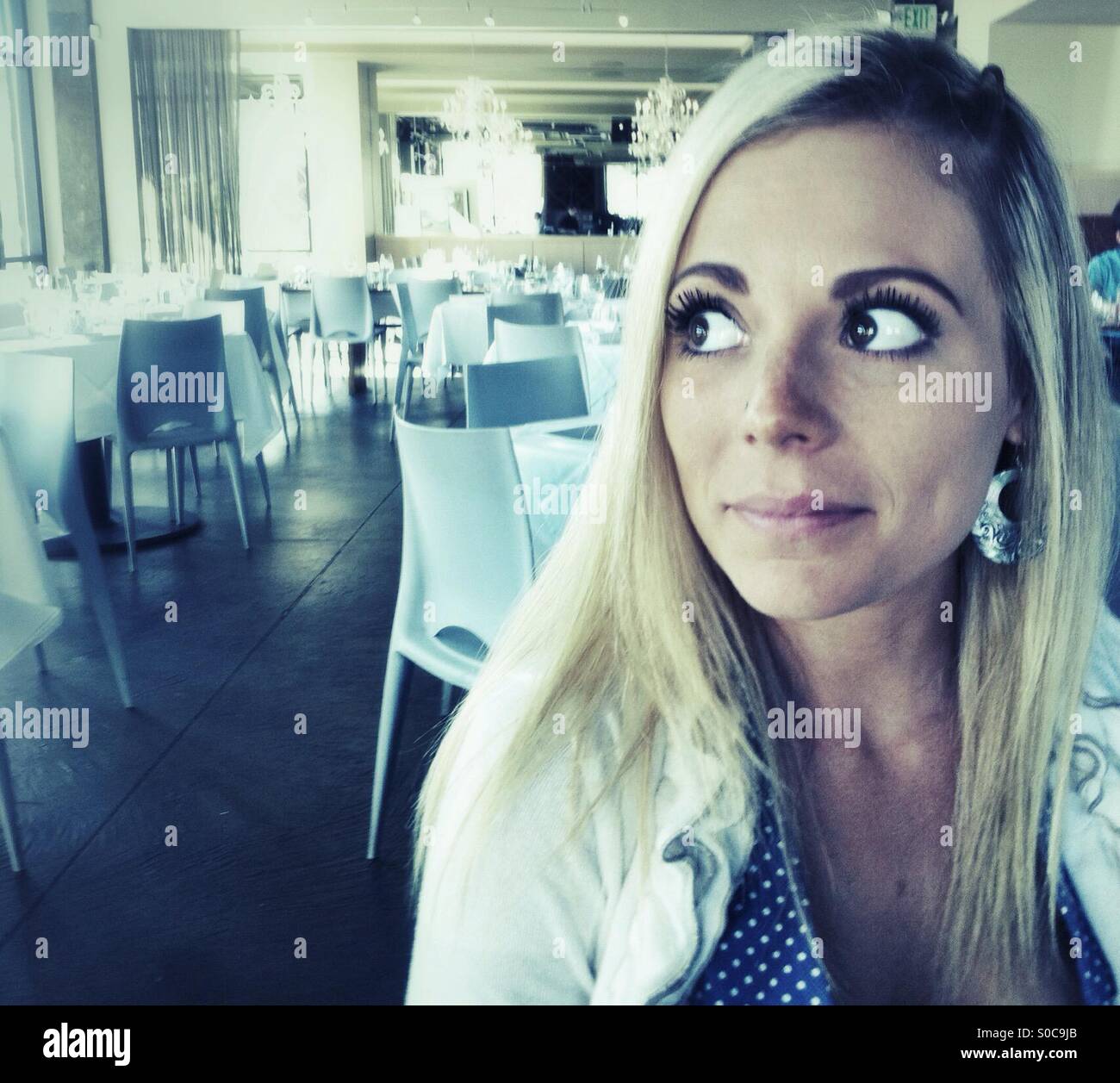 Young blond woman at the table in empty restaurant - Smartphone Captured Stock Image