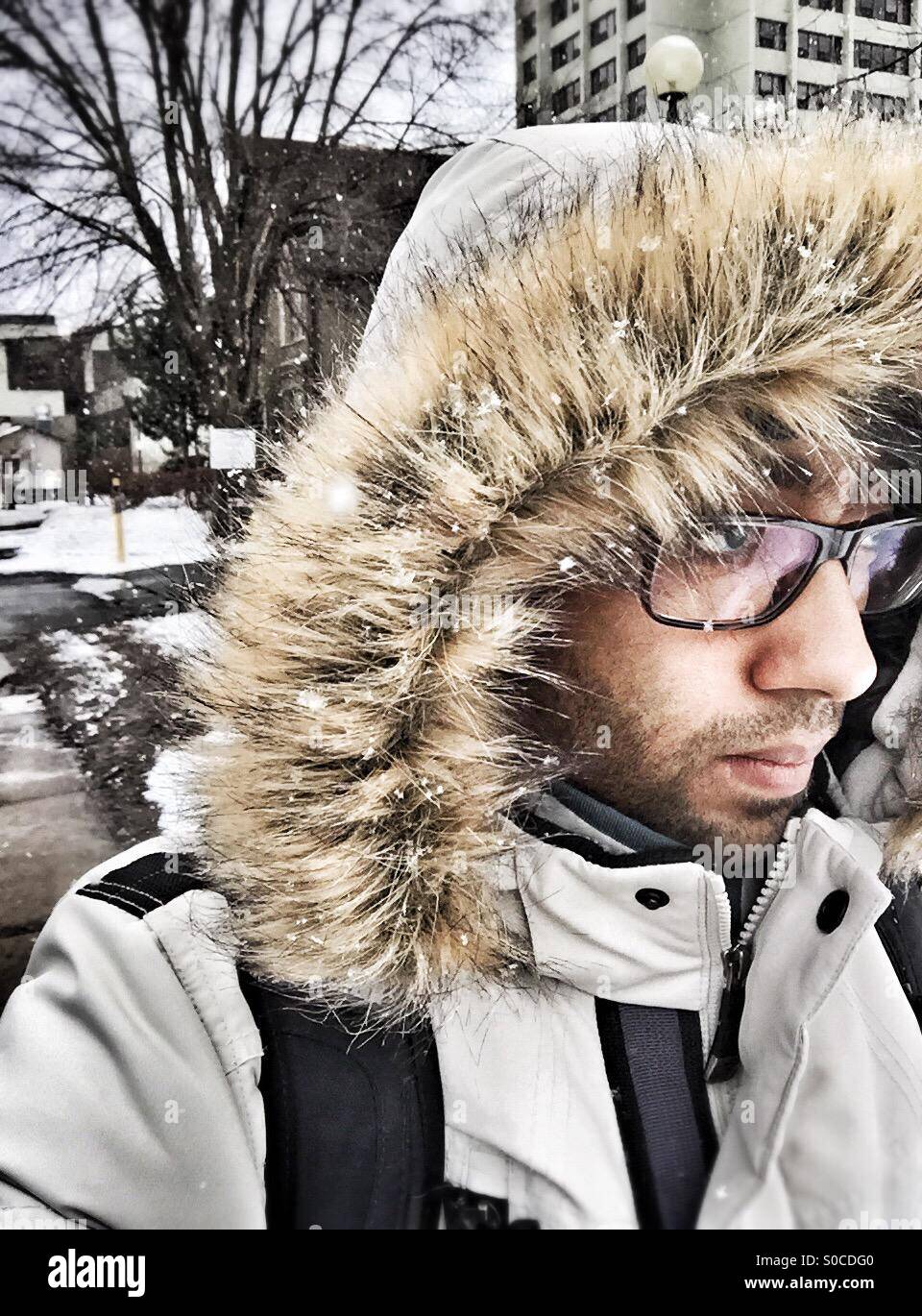 A guy walking outside in the snow, wearing winter coat with a fur hood. - Smartphone Captured Stock Image