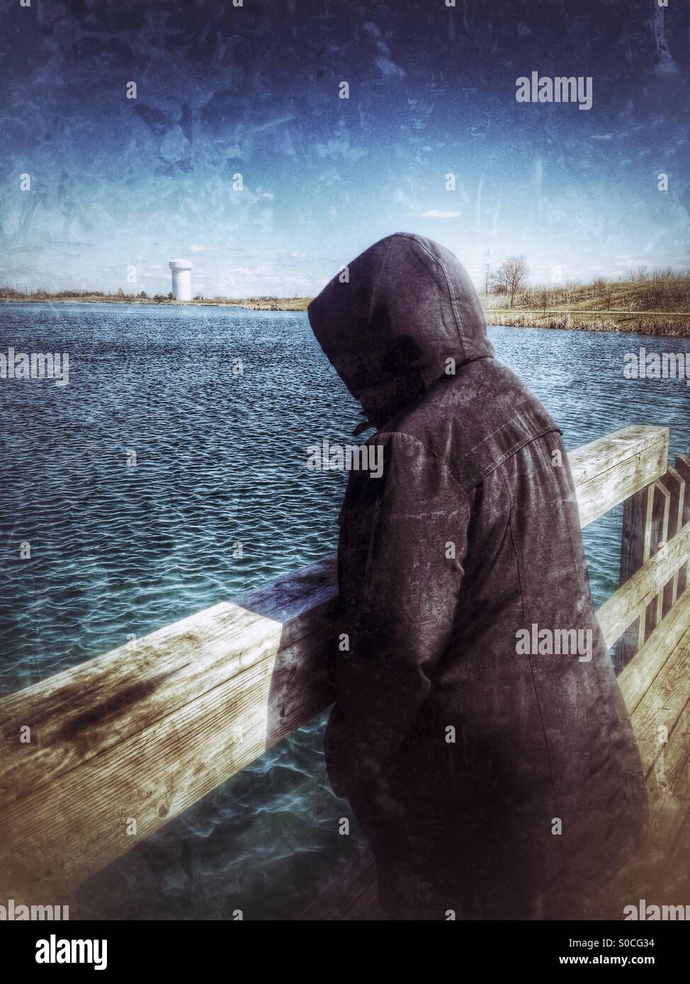 A lady with a black hooded jacket watching the ripples on a lake (1). - Smartphone Captured Stock Image