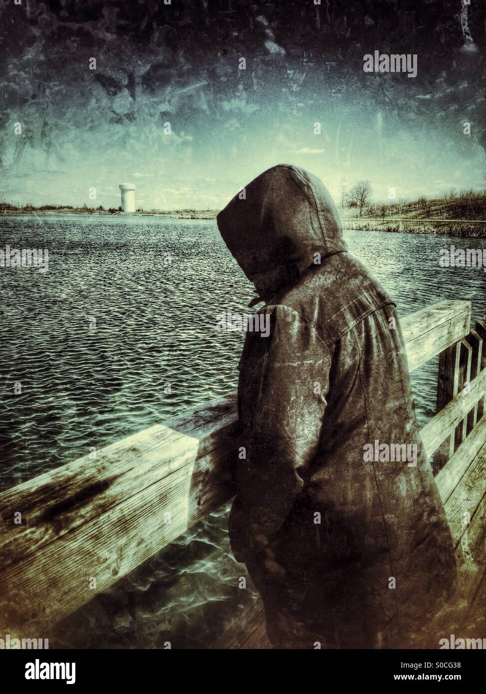 A lady with a black hooded jacket watching the ripples on a lake (3). - Smartphone Captured Stock Image