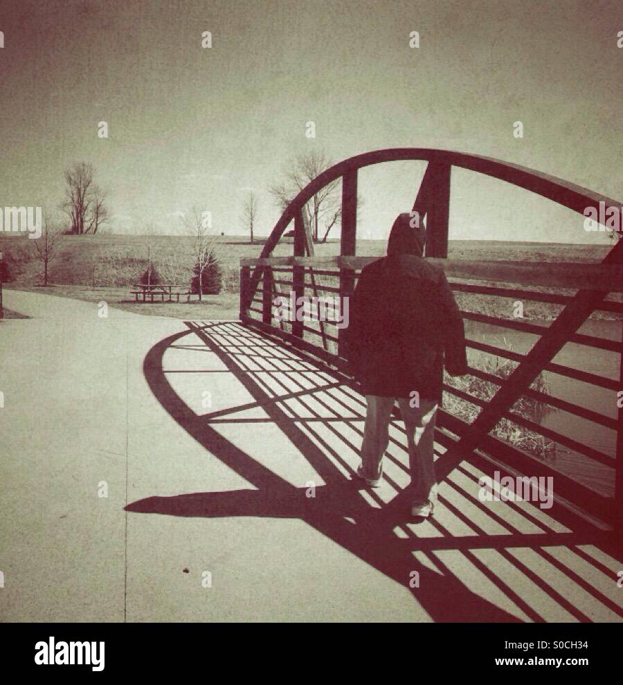 A lady with hooded jacket walking across a bridge (2). - Smartphone Captured Stock Image