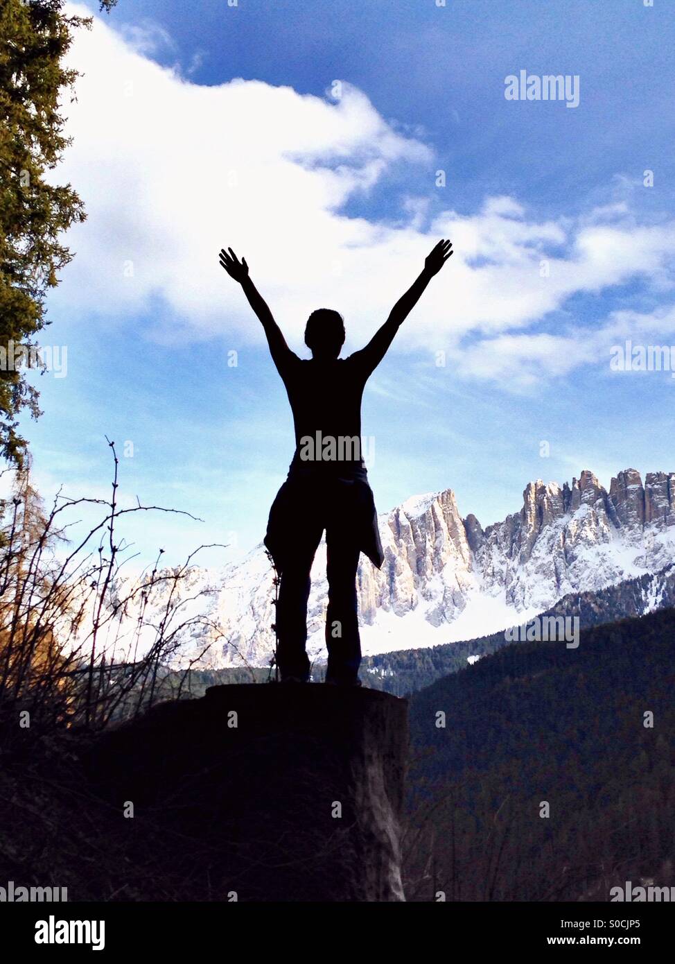 Young woman with arms raised in front of the Latemar Mountain covered by snow - Smartphone Captured Stock Image