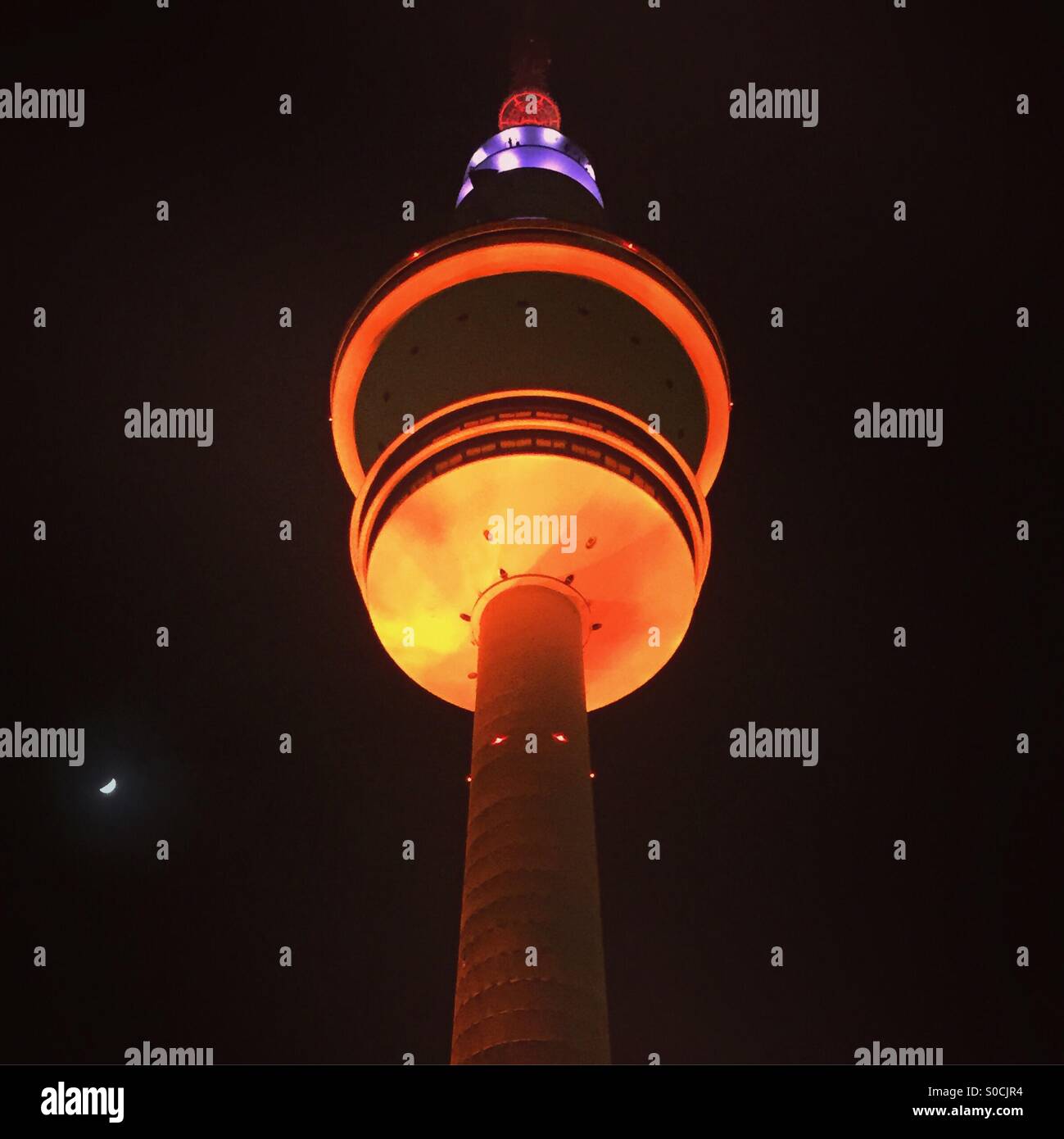 Hamburg's TV tower, the Heinrich Hertz Turm at night in front of the moon. Up-lit with orange and purple lights Stock Photo