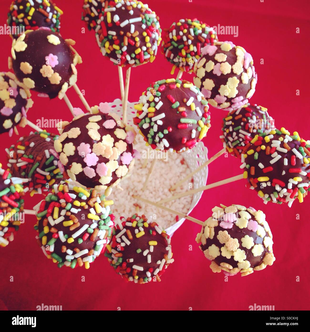 Many chocolate cakepops with sprinkles on red background Stock Photo