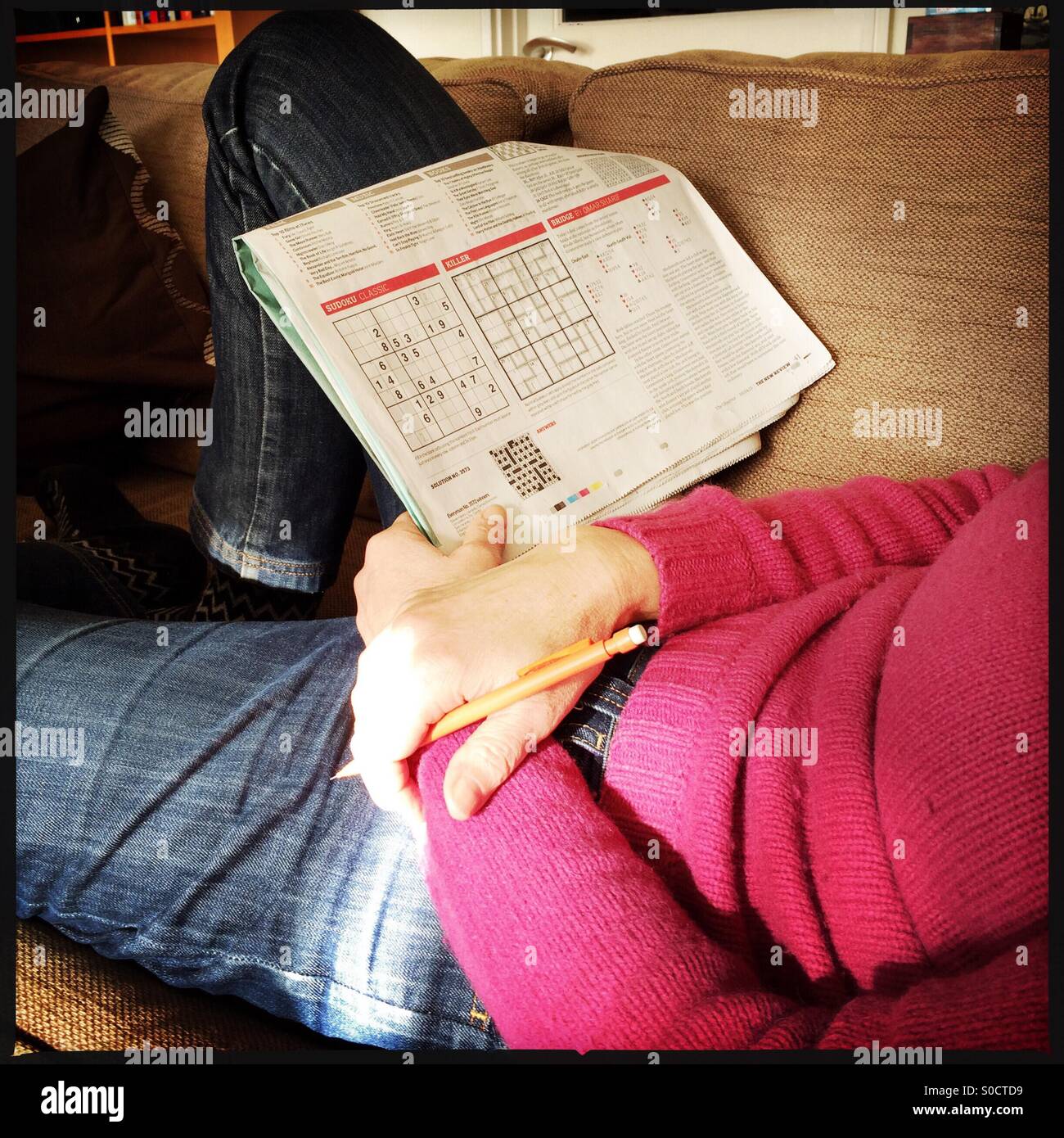 Woman relaxing at home doing sudoku puzzle - Smartphone Captured Stock Image