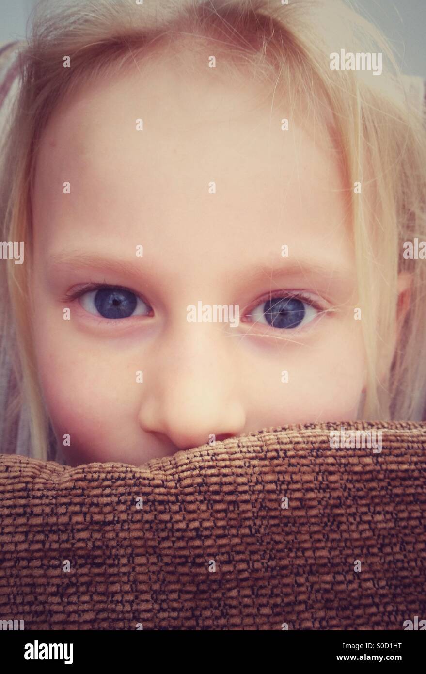 Young girl peering over cushion Stock Photo