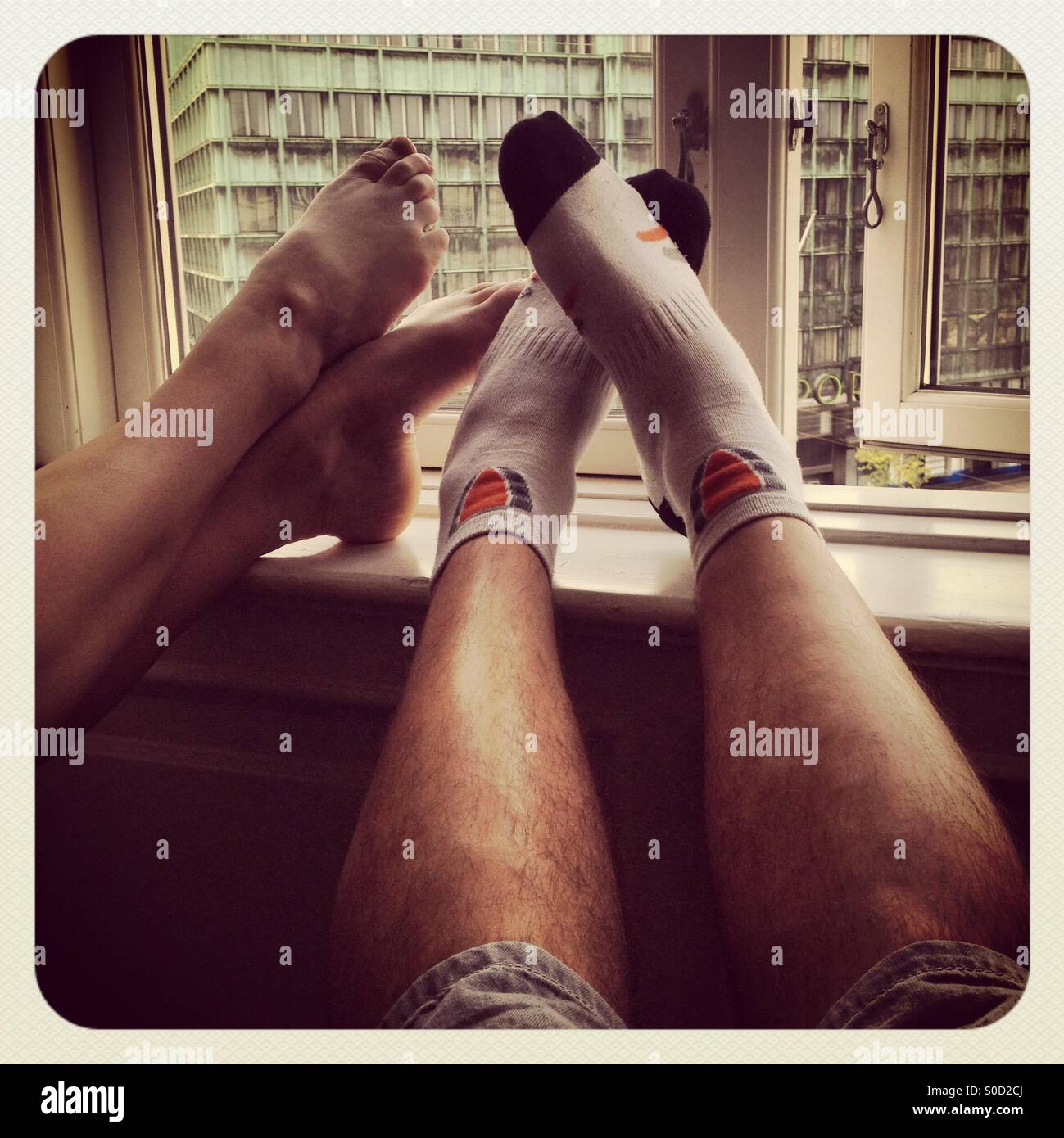 A couple resting their feet on a hotel window ledge at a hotel after a hard day's walking on a romantic city break in Copenhagen - Smartphone Captured Stock Image