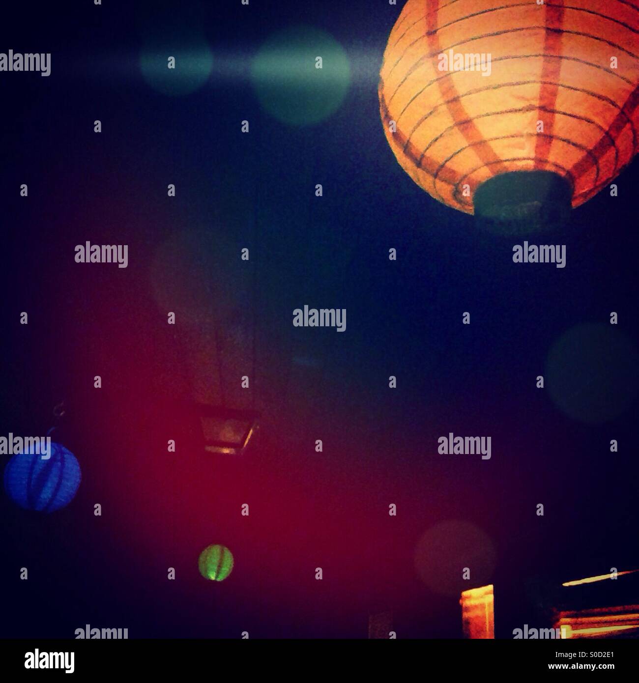 Orange, green, and blue paper lanterns glow against a dark backdrop