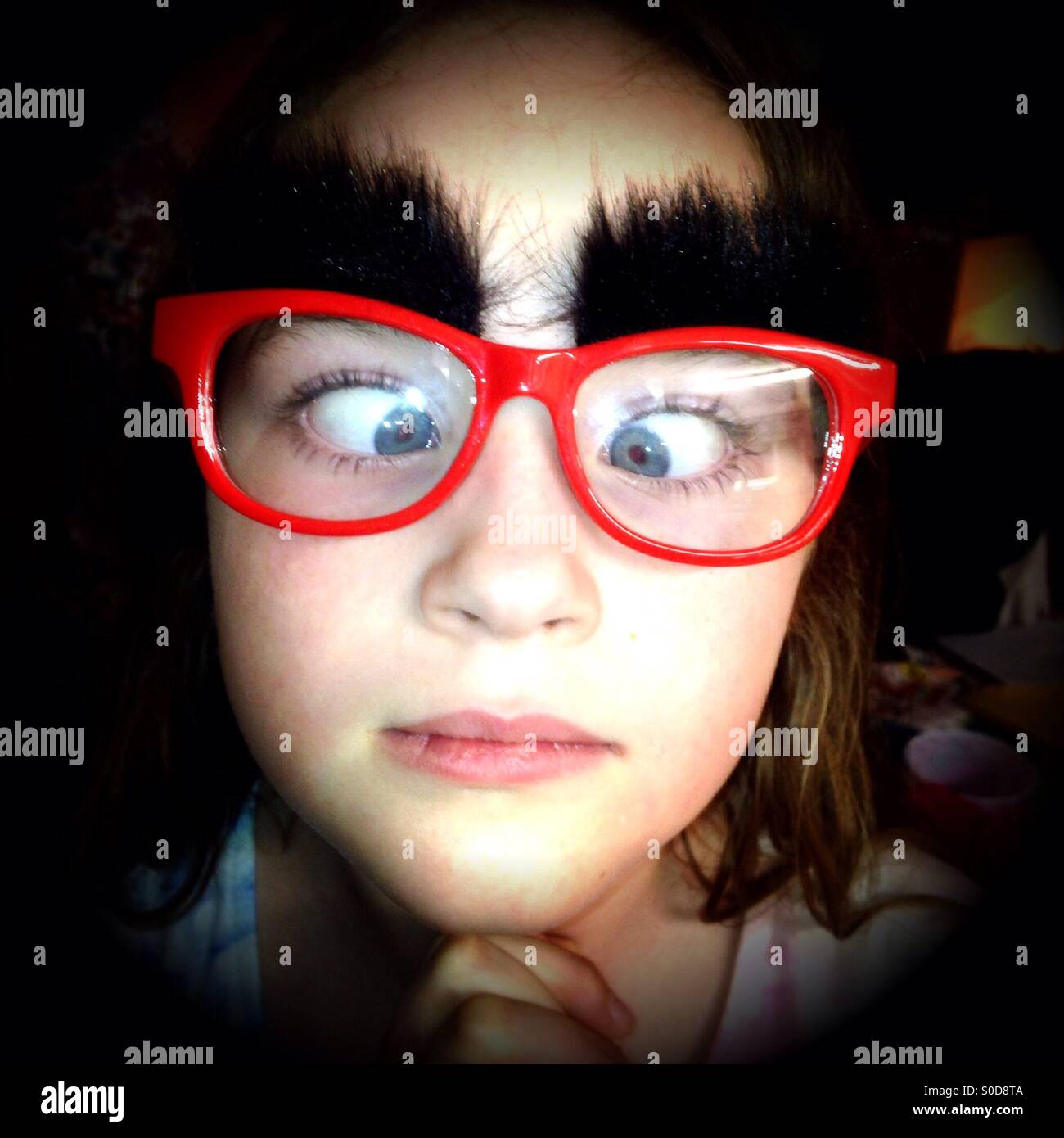 Young girl wearing red glasses with fake bushy eyebrows Stock Photo