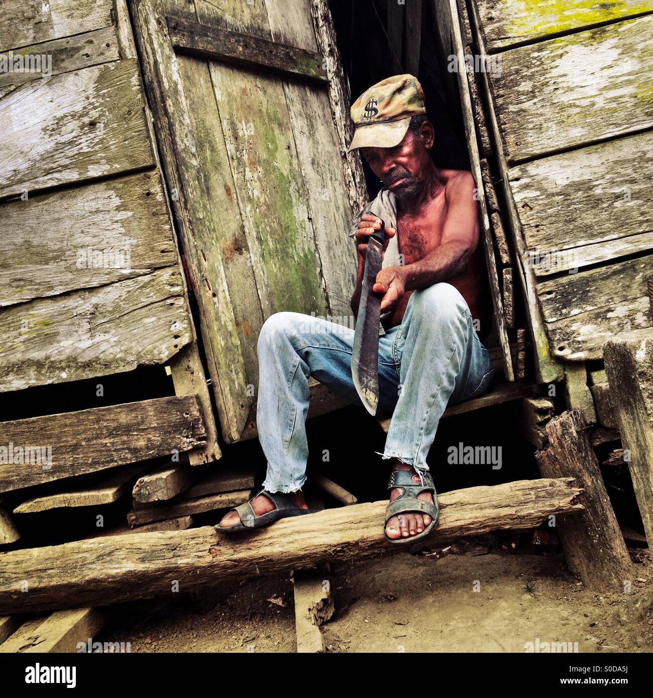 A Panamanian peasant checks the sharpness of the machete blade while sitting in the door of his house in Boca de Cupe, a community in the jungle region of Darién, Panama, 27 January 2015. Stock Photo
