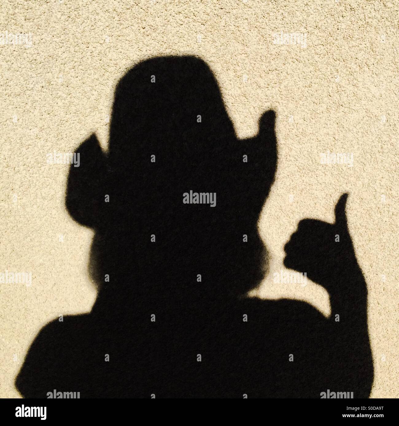 Shadow of a female wearing a cowboy hat with a thumbs up hand signal Stock Photo