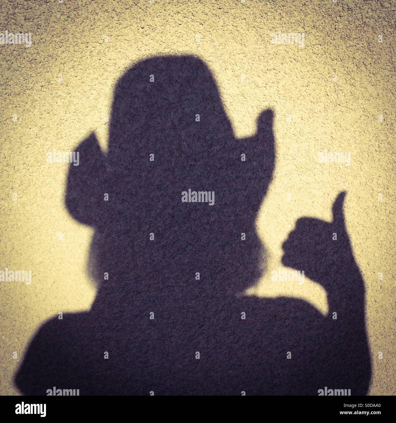 Shadow of a female wearing a cowboy hat giving a thumb's up hand signal Stock Photo