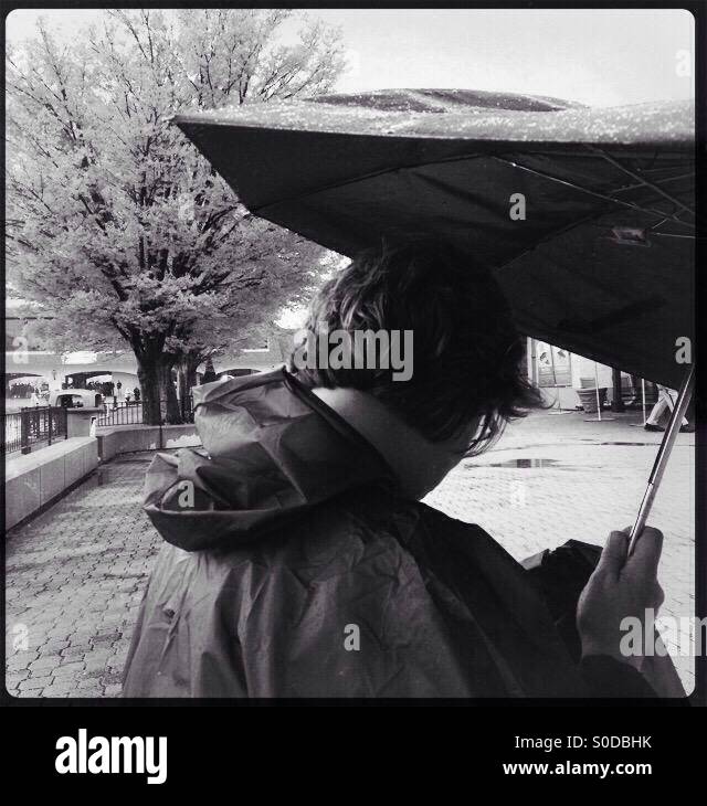 A lady holding an umbrella while checking text messages on her smartphone. - Smartphone Captured Stock Image