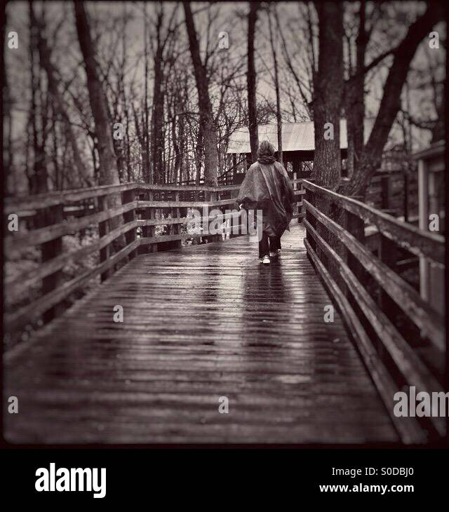 A lady dressed for rainy weather is walking across s wet bridge. - Smartphone Captured Stock Image