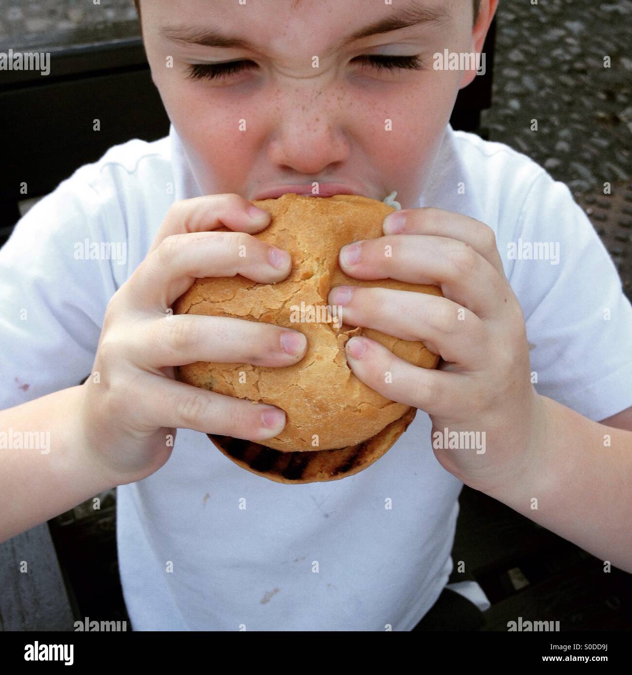 Six year old boy eating hamburger Stock Photo Alamy