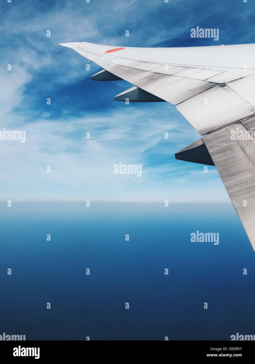 Window view of airplane wing of All-Nippon Airways Boeing 777-300 with blue sky and sea in background. Stock Photo