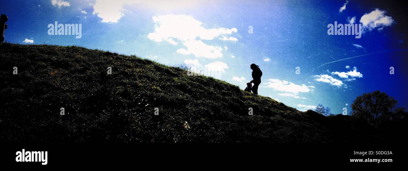Silhouette of adult and child climbing hill against blue sky Stock Photo