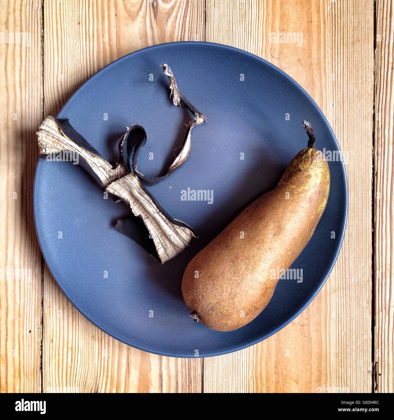 Pear and dry banana peel in a blue grey plate on a wood surface - Smartphone Captured Stock Image