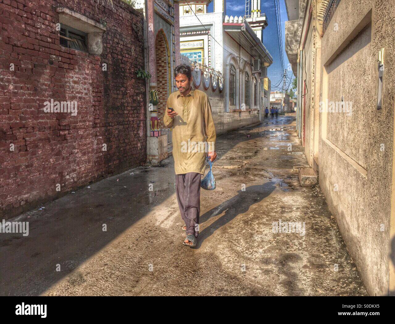 Man texting on mobile phone as he walks in the street , Kharian village Pakistan - Smartphone Captured Stock Image