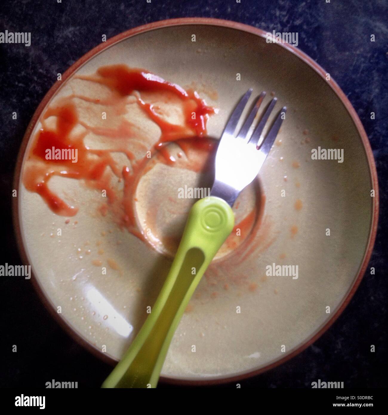 A dirty plate with tomato ketchup left on the side. Stock Photo