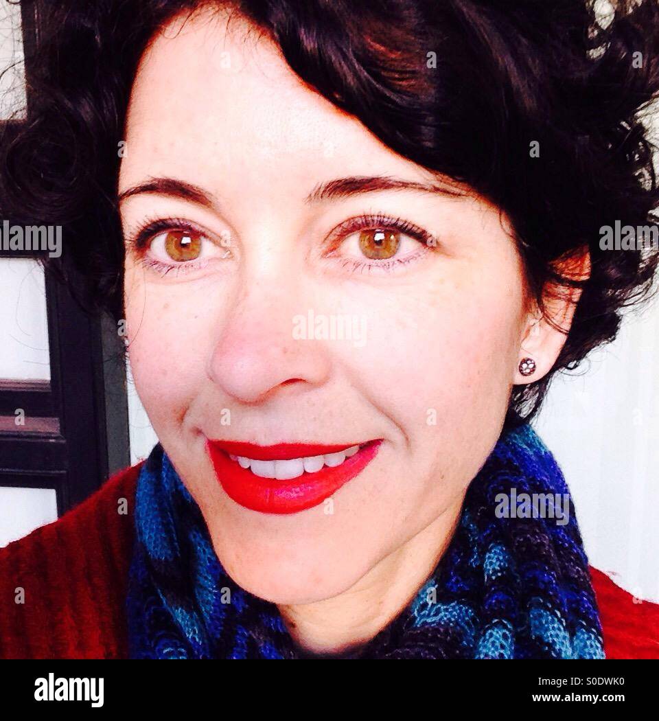 Woman wearing red lipstick with blue scarf and red coat smiling at friend - Smartphone Captured Stock Image