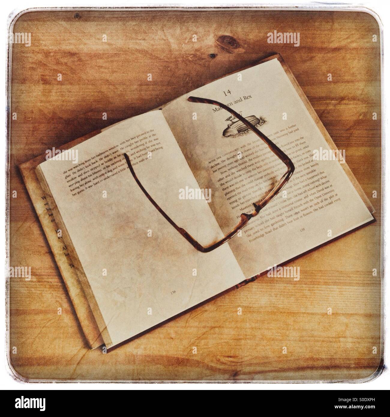 Hardback book, with a pair of reading spectacles on top, on a wooden desk - Smartphone Captured Stock Image