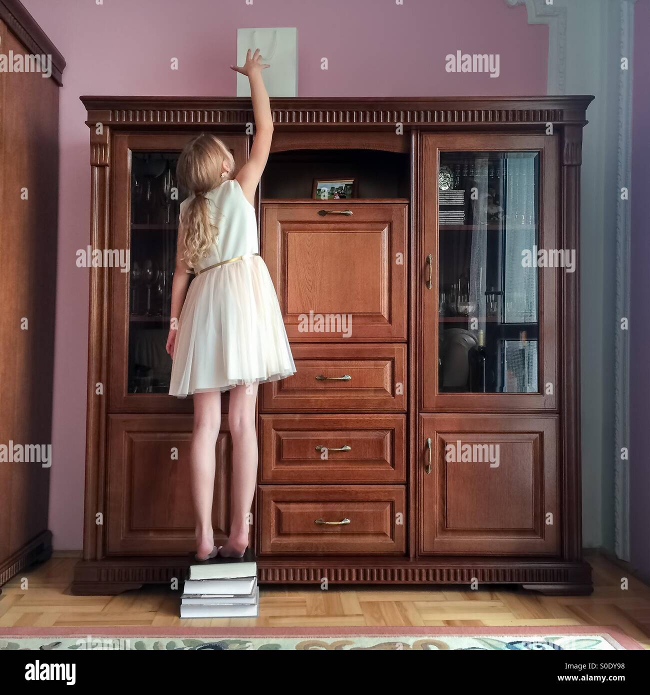 Young girl reaching the bag with a gift put high on the cupboard Stock