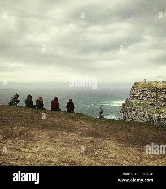 Young tourists sitting on the edge of a rock at Cliffs of Moher, County Clare, Ireland. - Smartphone Captured Stock Image