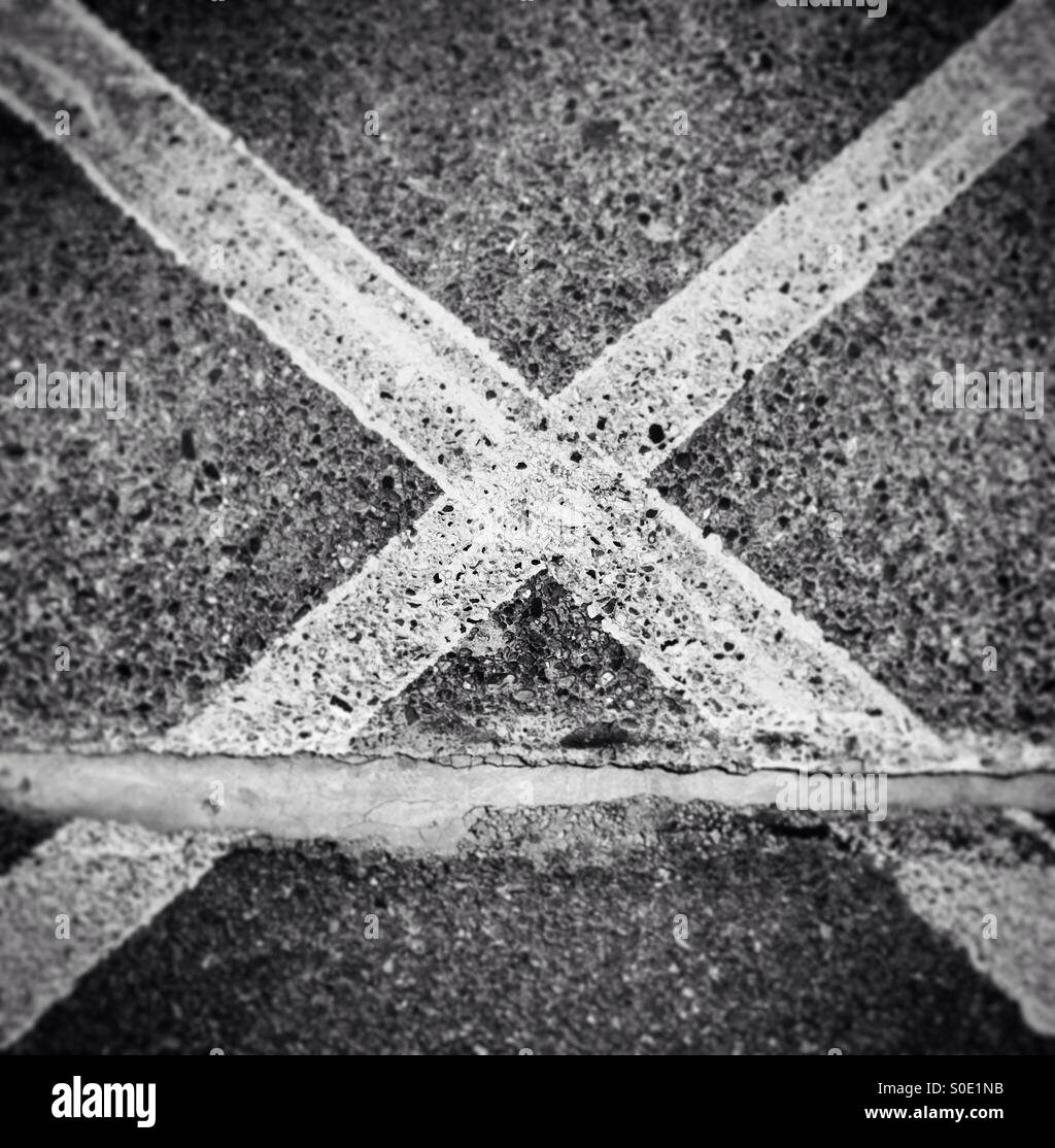 Black and white photo of a painted cross on a train platform floor - Smartphone Captured Stock Image