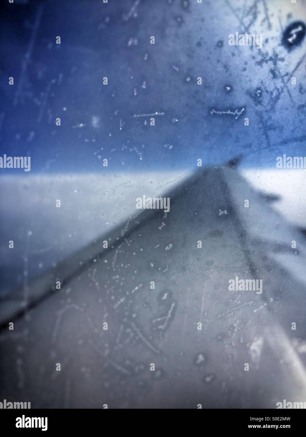View over wing of passenger aeroplane, dramatic treatment, scratched, frosted window. Stock Photo