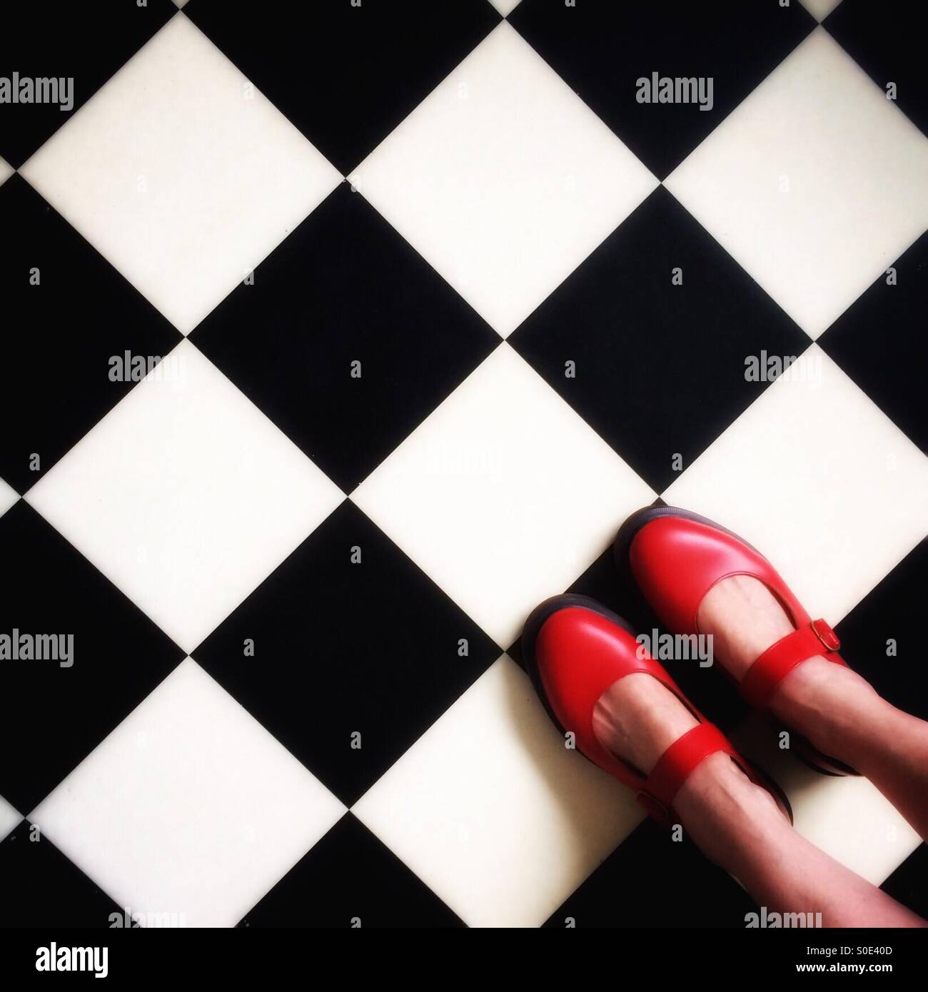 Dr Marten red leather Mary Jane style shoes on a black and white square patterned retro style floor. Stock Photo